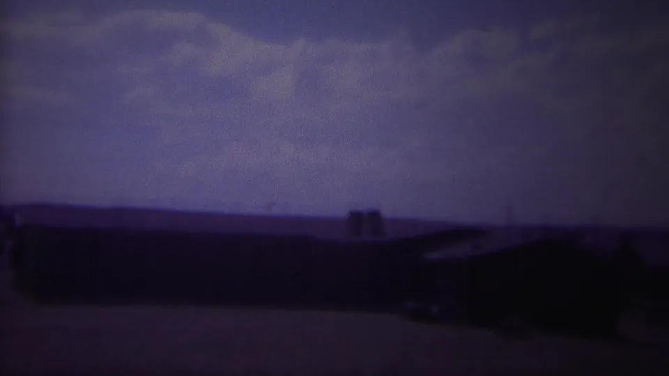 A dark, grainy 1967 Yellowstone-area frame with low rooflines, open ground, and a clouded purple-blue sky.