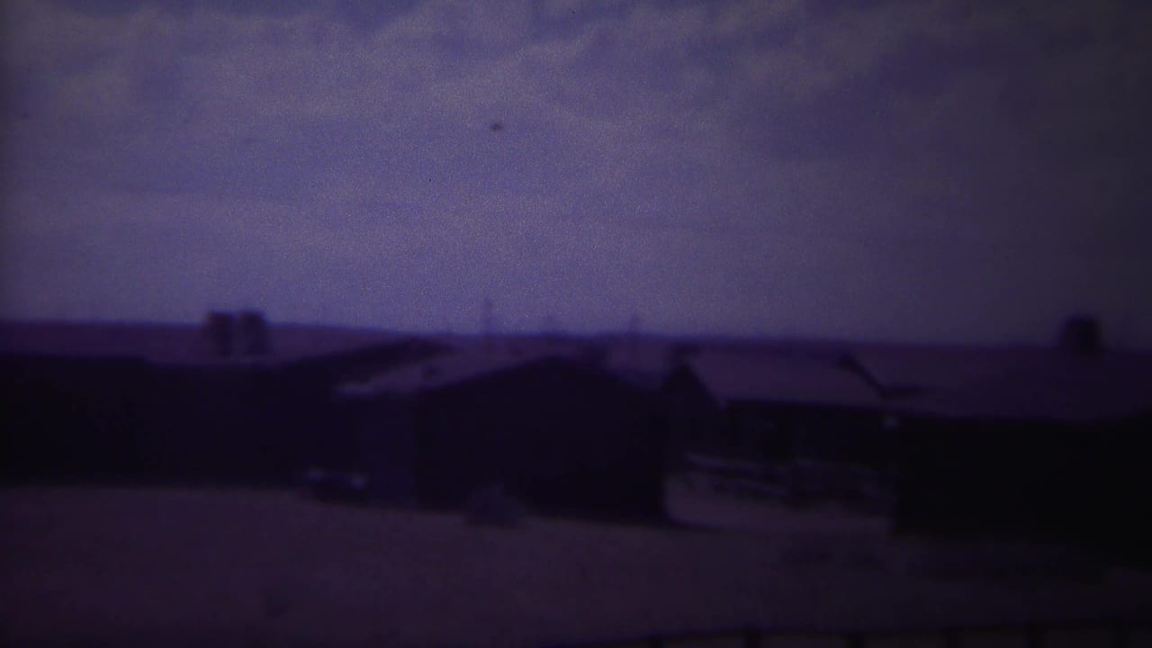 Soft 8mm view of low wooden buildings under a pale sky.