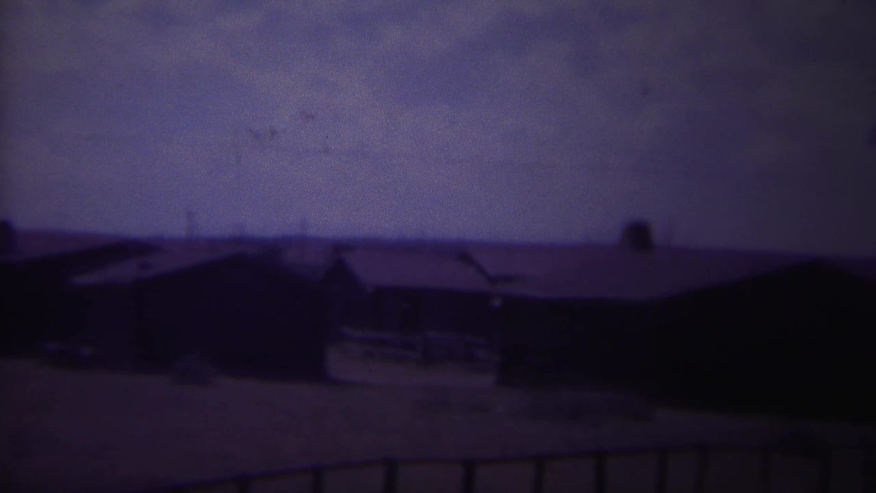 Dark-roofed buildings and open ground seen through aged film color.