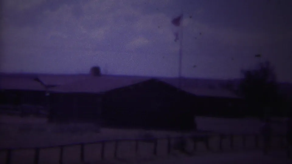 1967 home-movie view of a flagpole near low buildings and a foreground fence in Yellowstone, Wyoming.