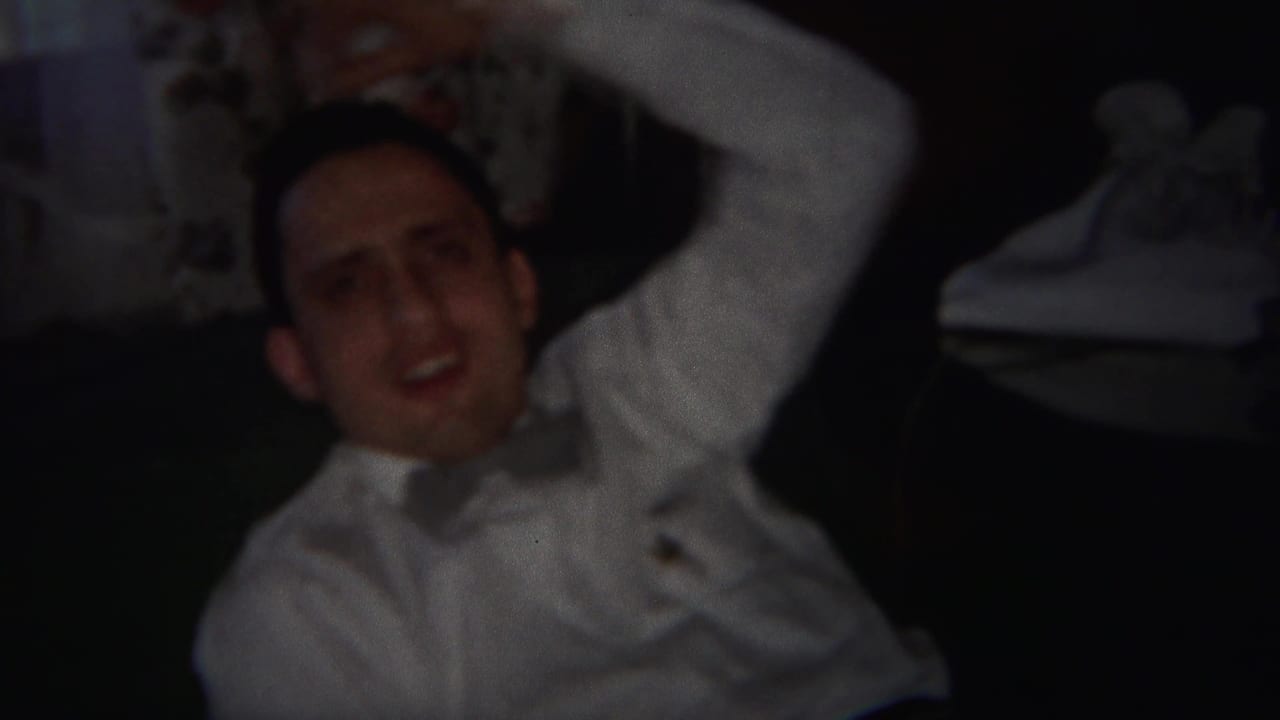 Man in a white shirt reclines indoors with one arm behind his head.