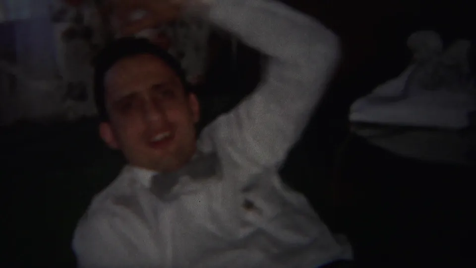 In the Westville, New Jersey home-movie footage, a man in a white shirt laughs while reclining in a dim room.