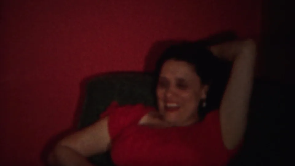 A woman in a red dress smiles with one arm behind her head in the 1951 Westville home interior.