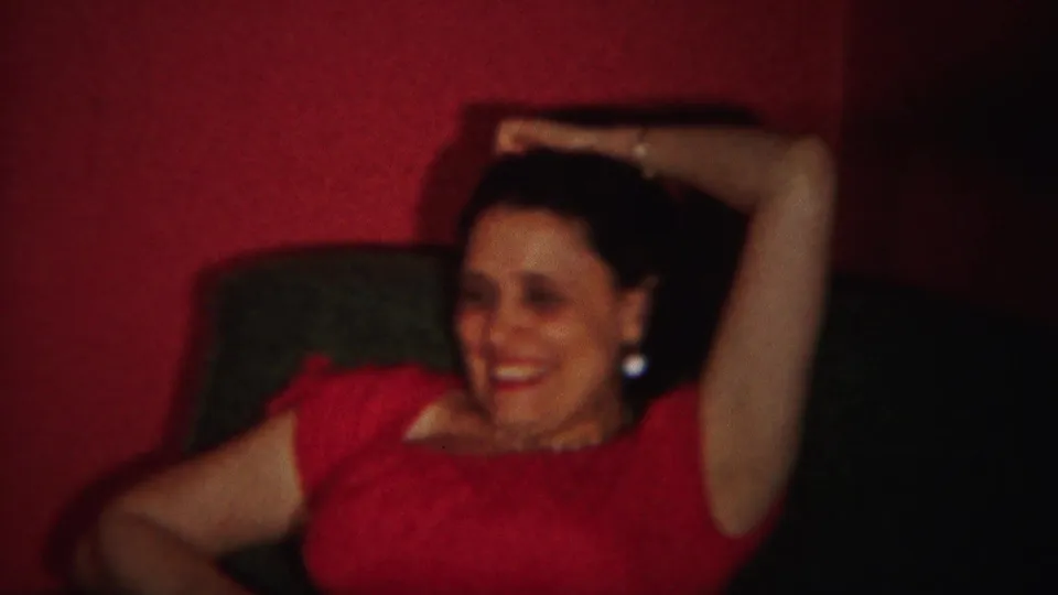 The woman in red laughs in soft 8mm focus, framed close against the red-walled private interior.