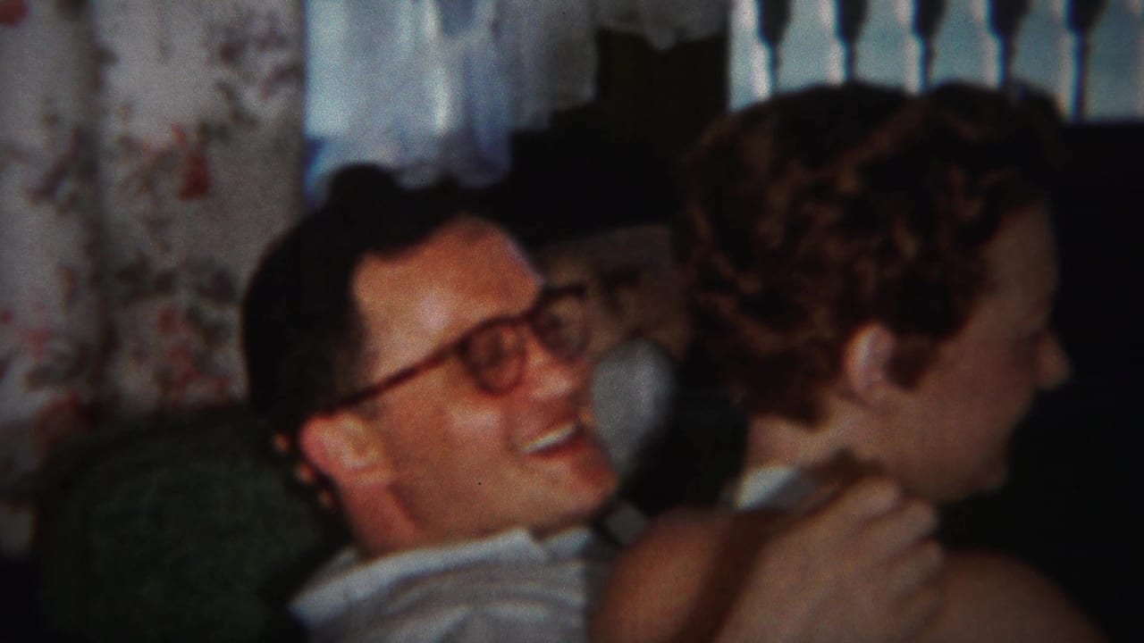 Man in glasses embraces a woman from behind on a living-room seat.
