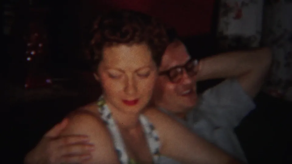 The woman looks downward as the man reclines behind her with an arm raised in the living-room home movie.