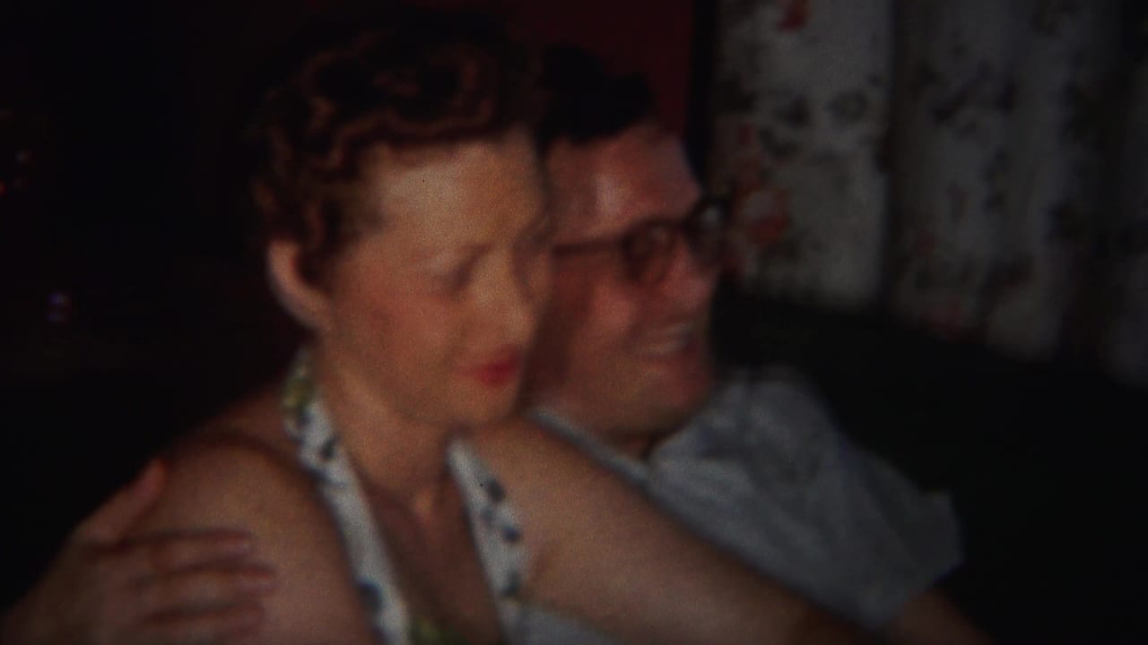 Woman and man sit close together on a couch in a dim room.