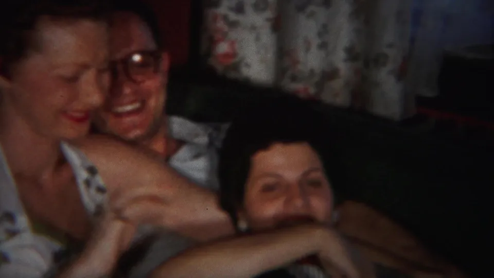 Three adults sit close together on the couch in the supported 1951 Westville home movie, with smiles and floral curtains visible.