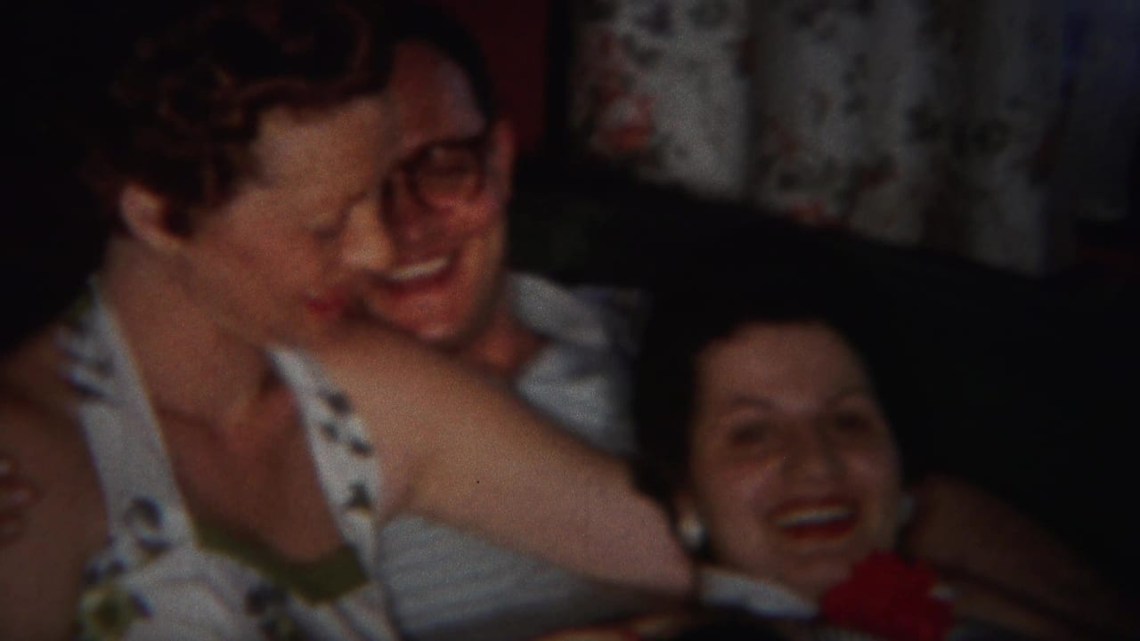 Two women and a man with glasses laugh together while seated close on a couch.