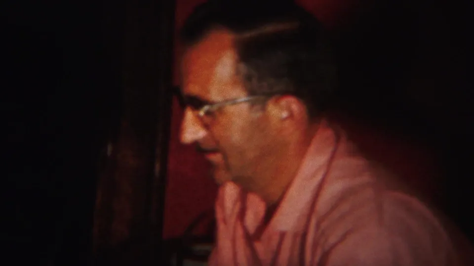 The man in glasses and a pink shirt looks downward in the red-walled Westville interior, captured with soft 8mm focus.