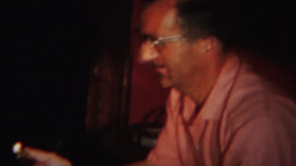 In 1951 Westville home-movie footage, a man in glasses and a pink shirt smiles while seated in a low-lit room.