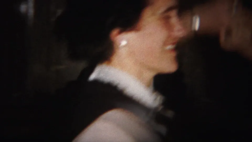 A young woman in a dark dress with a white ruffled collar smiles in profile while dancing in the 1951 Westville home movie.