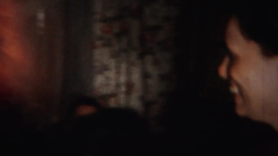 1951 Westville, New Jersey home-movie frame showing a dim indoor party with a woman in profile and other women partly visible nearby.