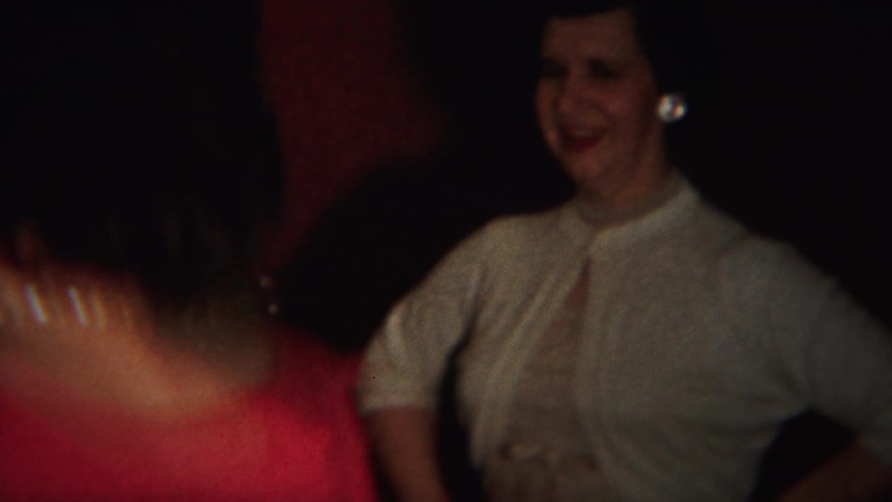 Woman in a red dress passes in front of a smiling woman in a light top.