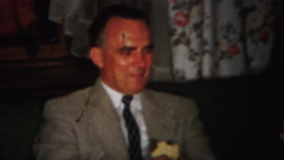 1951 Westville frame showing a seated man in a light suit and dark tie holding a small piece of food in a home interior.