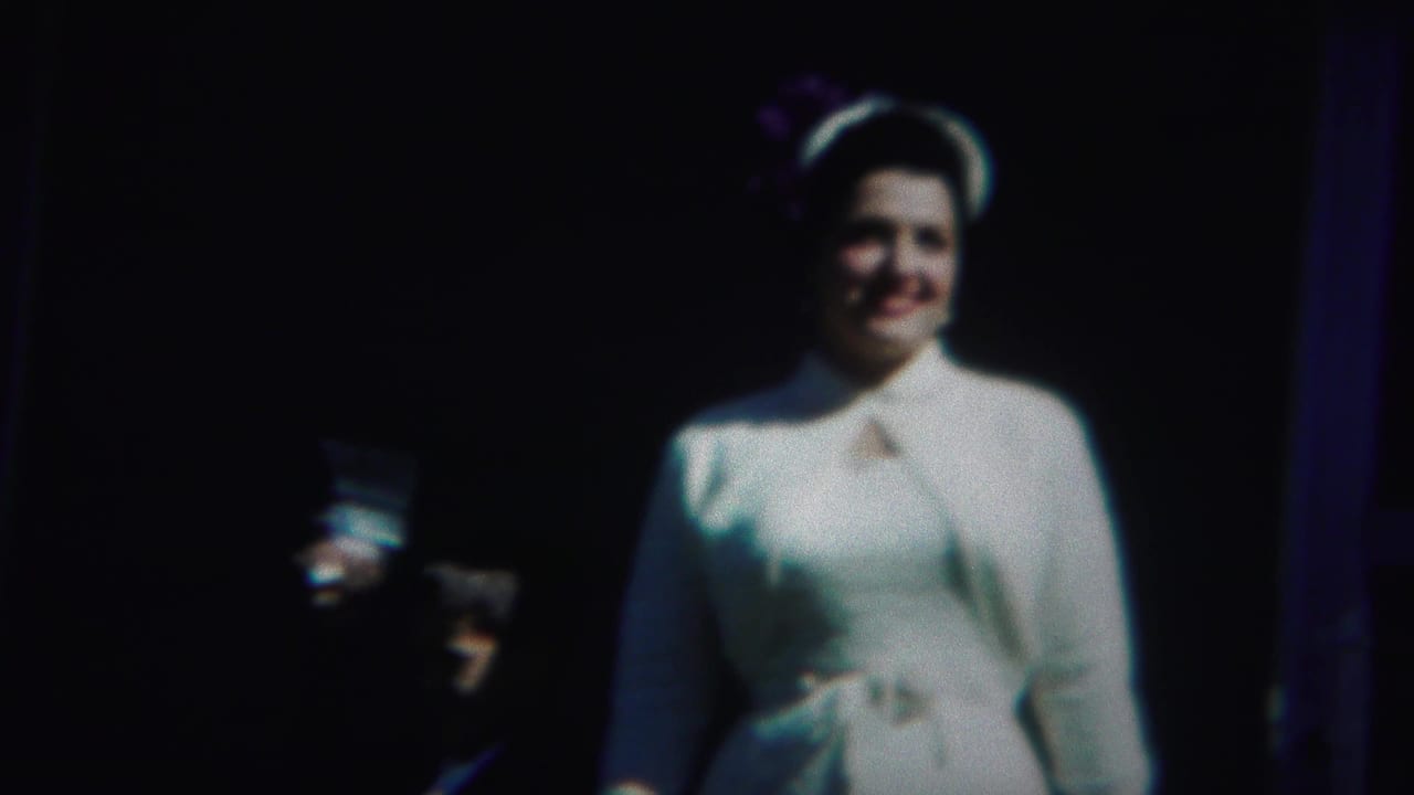 Woman in a white dress and hat smiling in strong light against a dark background.