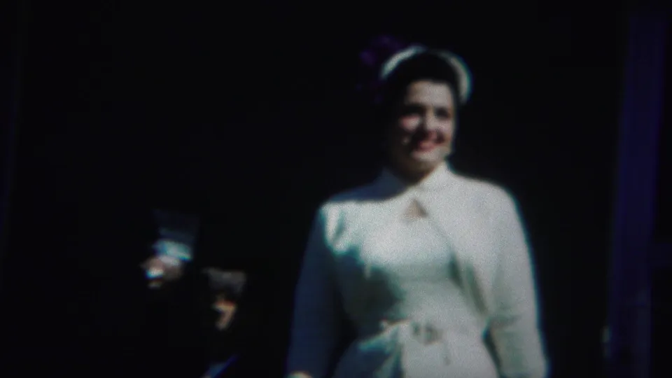In 1951 Westville, New Jersey footage, a woman in white formal clothing smiles toward the camera against a shadowed backdrop.