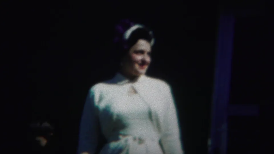 The woman in white formal attire appears in soft 8mm focus, turned slightly beside a dark doorway or post in the 1951 Westville footage.