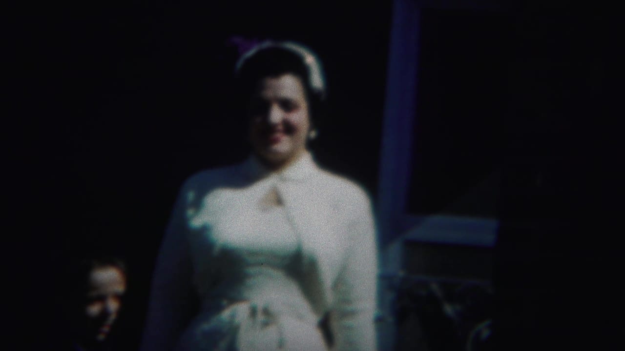 Woman in a white dress and hat smiles while a partially visible face appears nearby.