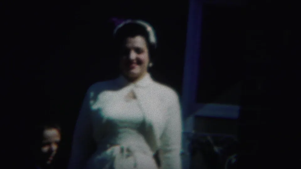 In the Westville, New Jersey 1951 clip, the woman remains centered in a white dress and hat with another face partly visible behind her.