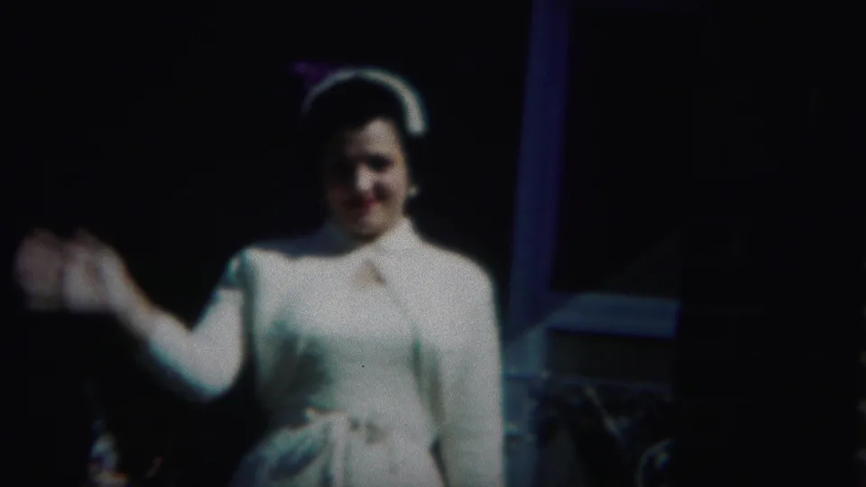 The woman in the 1951 Westville home movie lifts one hand in a friendly wave while wearing a white dress and hat.