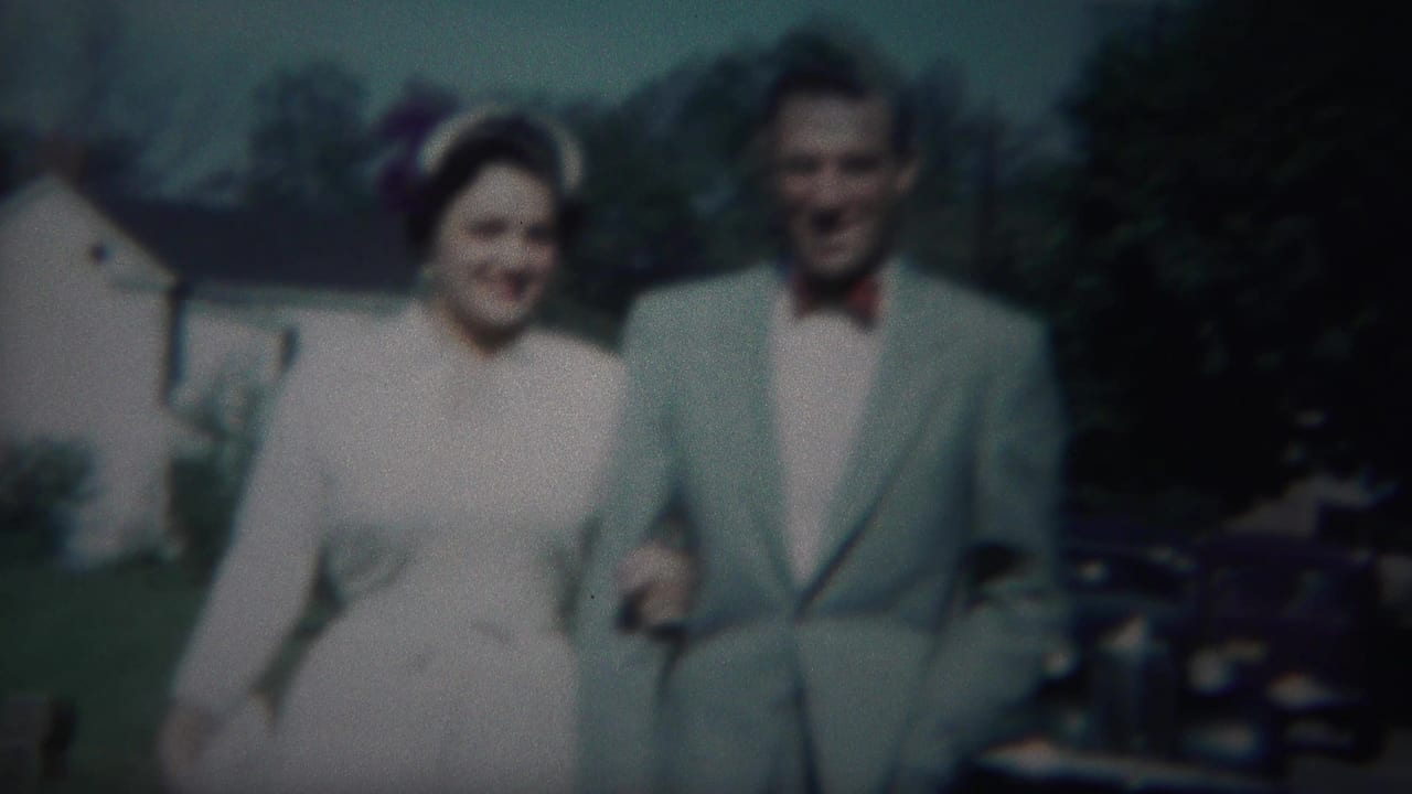 Smiling bride and groom walk arm in arm with trees and parked cars behind them.