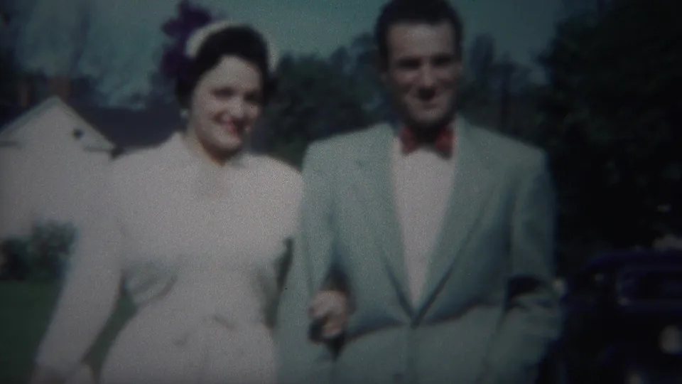 Closer 8mm frame of the 1951 Westville newlywed couple walking toward the camera in formal attire.