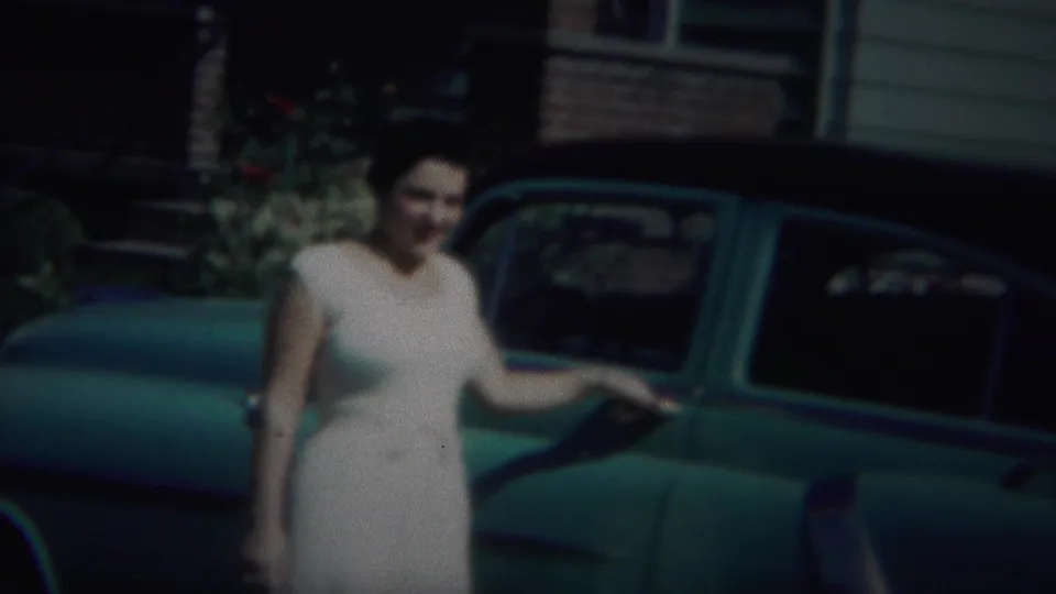 The final frame keeps the woman and green vintage car in view, with the residential exterior and garden plantings still visible behind them.