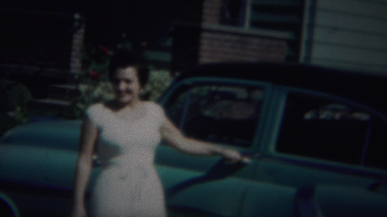 Woman smiles beside a parked teal car with her hand near the door handle.