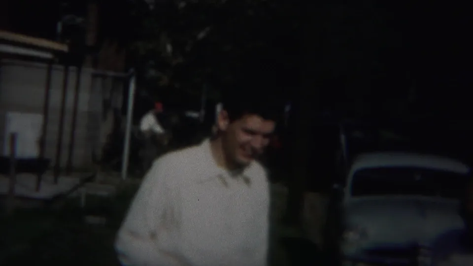In 1951 Westville, New Jersey footage, a man in a white shirt appears near a shaded street with mid-century cars in the background.