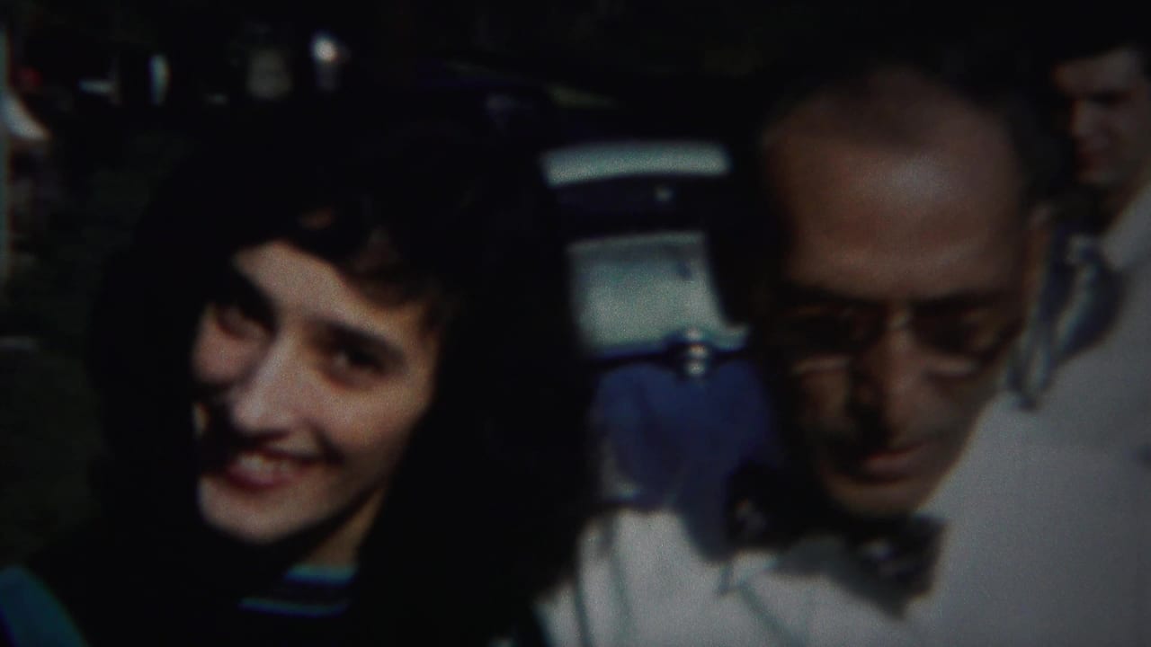 Young woman smiles beside an older man in glasses and a bow tie outdoors.