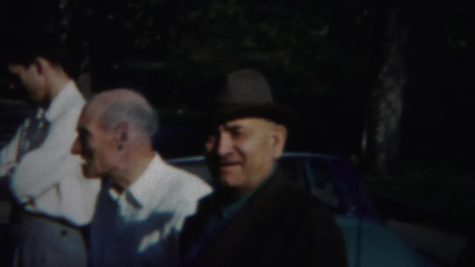 A fedora-wearing man smiles beside a blue-green car while other men stand close by in the 1951 Westville home-movie scene.