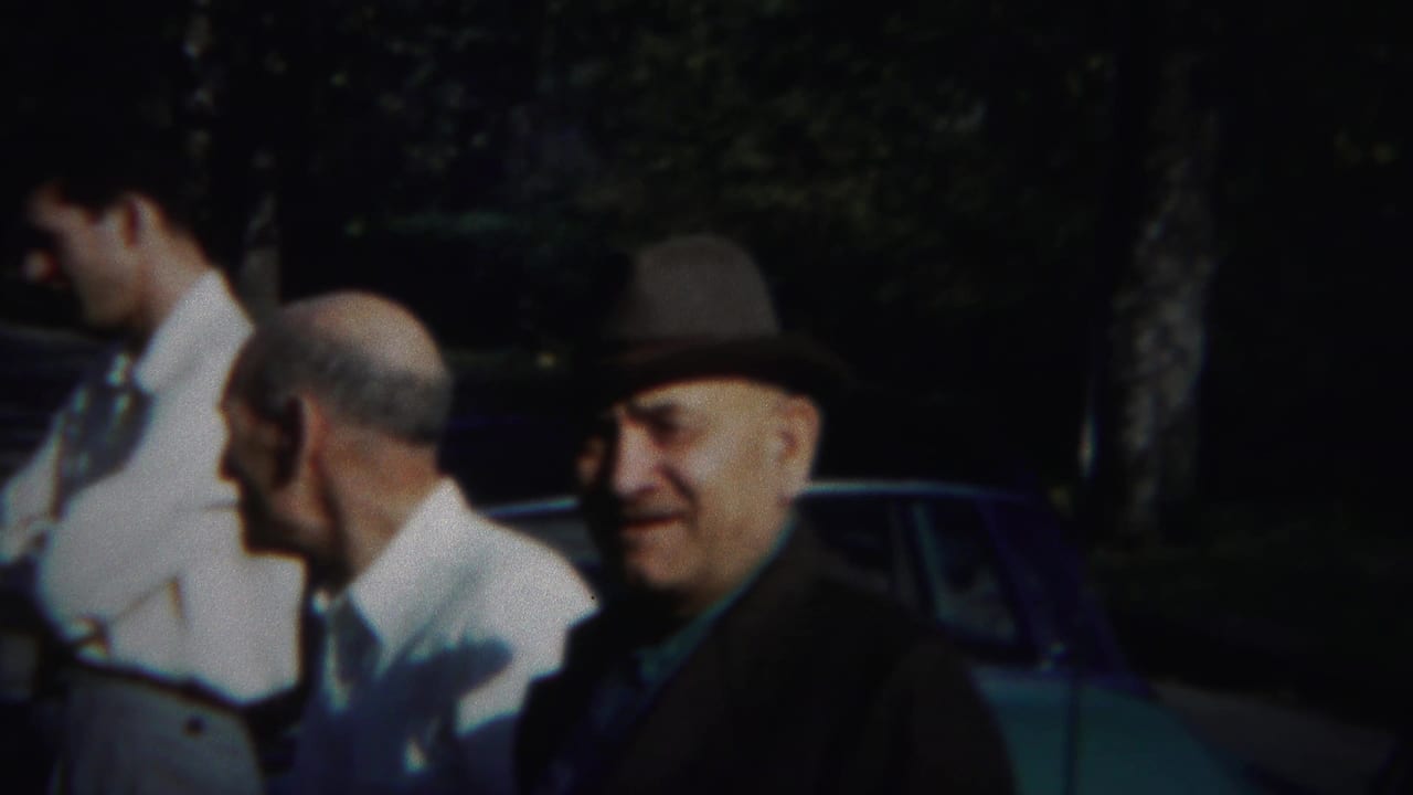 Three men standing outdoors near a parked car and trees.