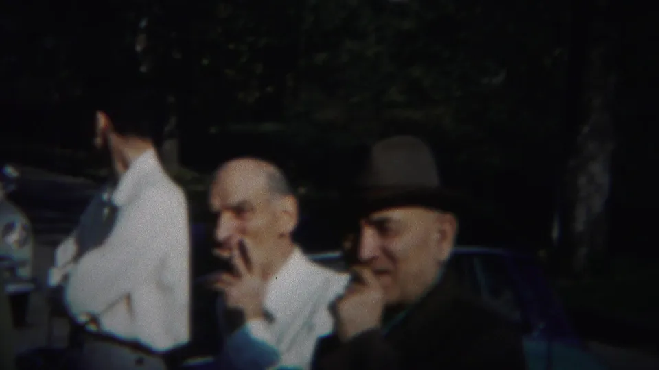 1951 home-movie frame from Westville showing two older men gesturing in conversation while another man stands beside a parked car.