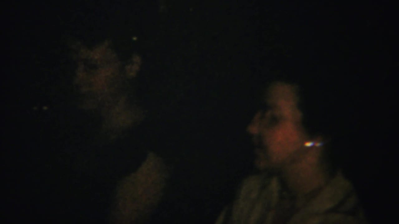 Low-light 1951 home-movie frame with adults gathered indoors, including a woman in profile at the right edge.