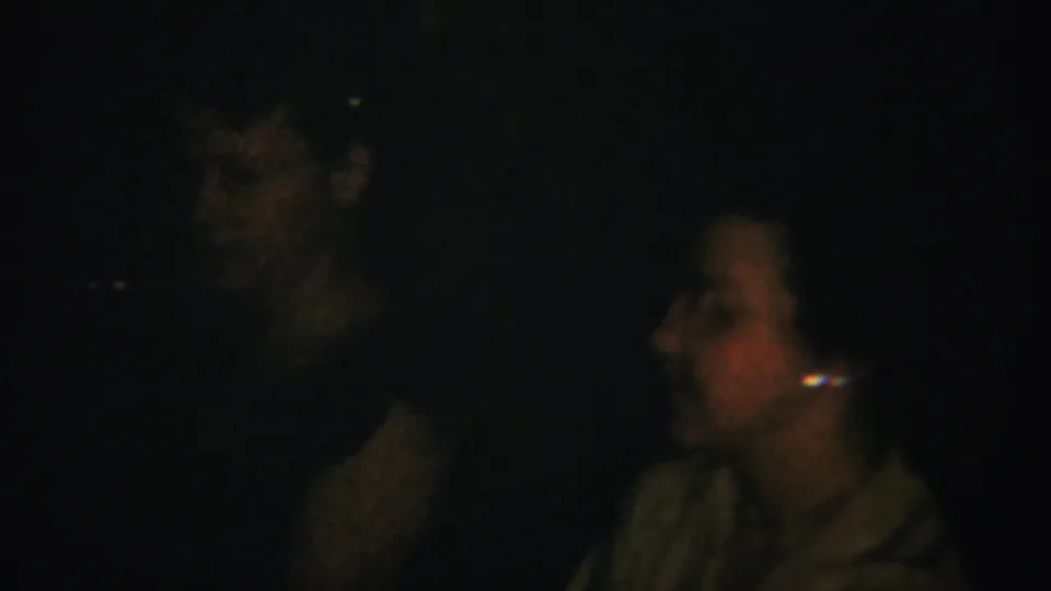 Low-light 1951 home-movie frame with adults gathered indoors, including a woman in profile at the right edge.