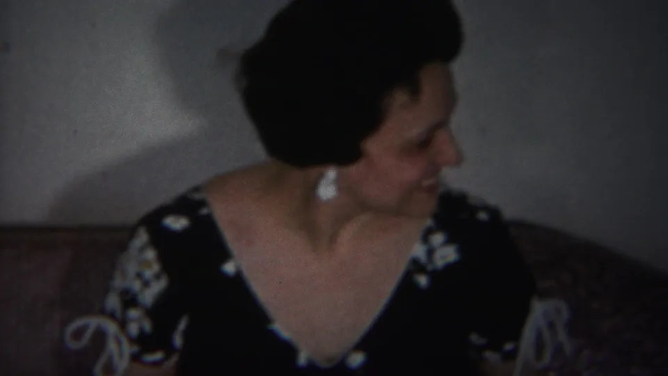 The woman turns sideways with a smile in the supplied 1951 Westville home-movie footage, seated against a wall in a private room.