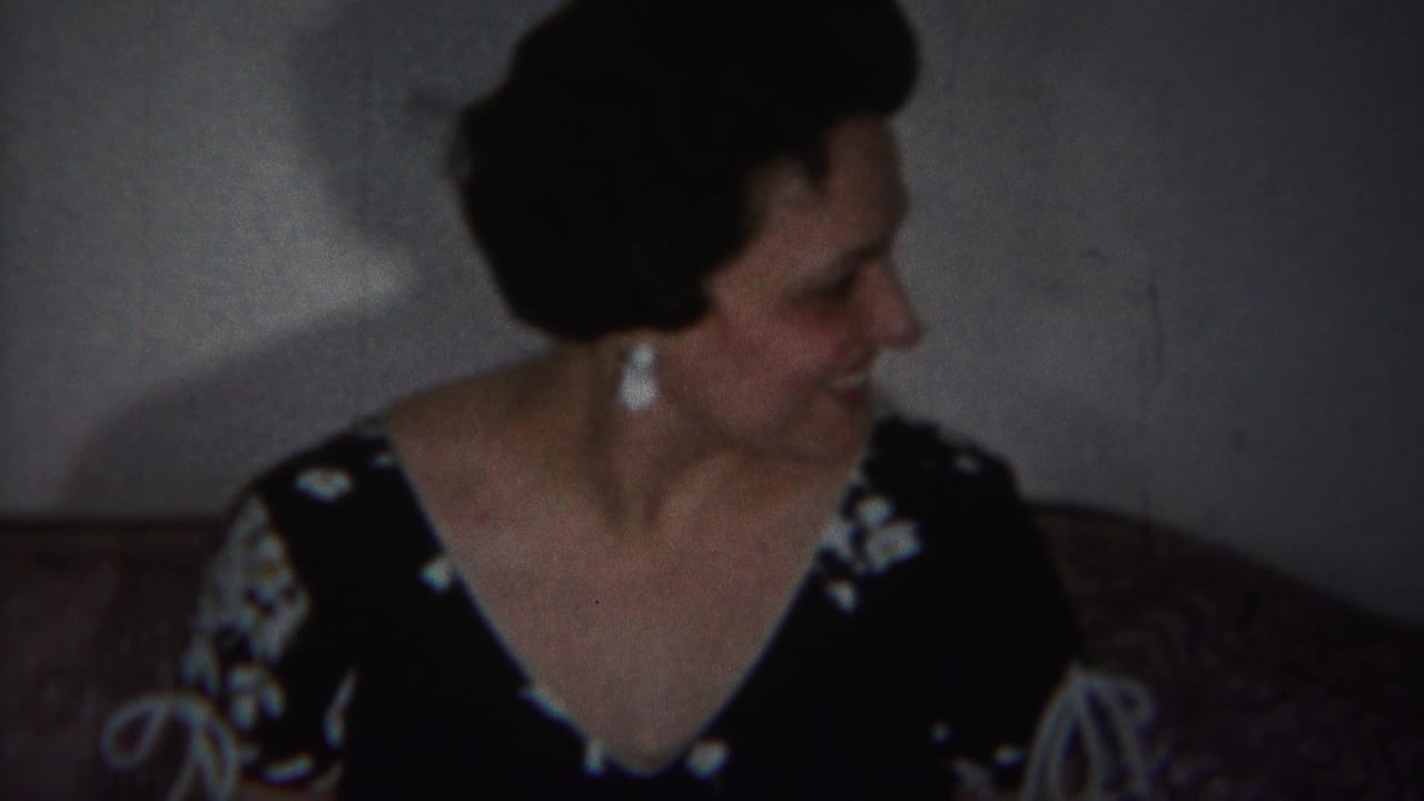 Woman in a dark floral dress smiles while seated on a patterned couch.