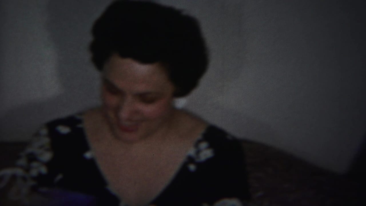 Two women seated indoors, one looking down in a dark dress.