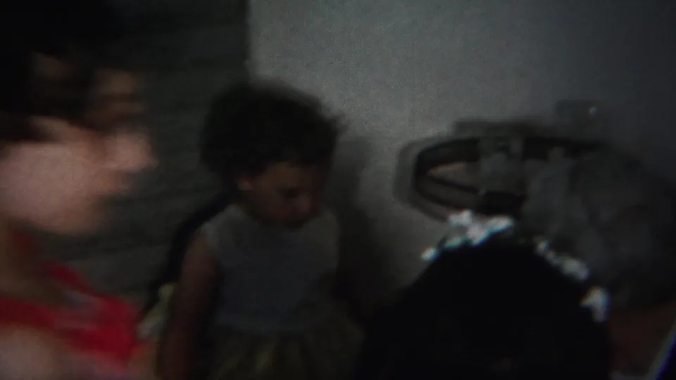 1951 Westville home-movie frame showing several people in a dim private room, including a small childlike figure near metal furniture.