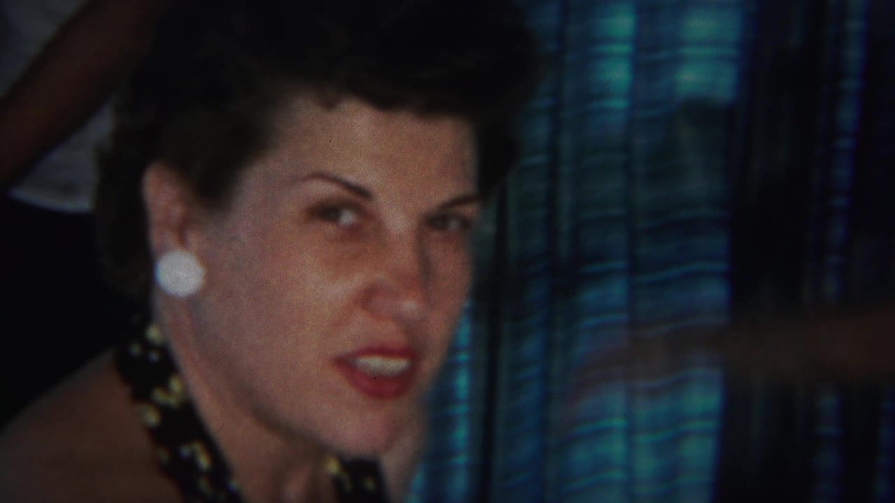 Woman with dark styled hair and white earrings seated before blue striped drapes.