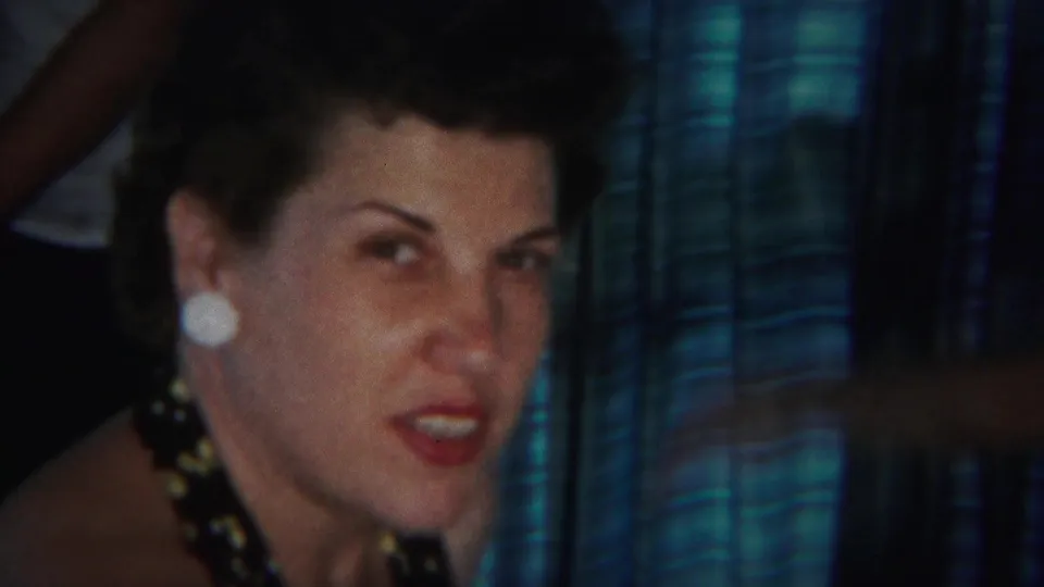 In 1951 Westville home-movie footage, a woman with dark styled hair, white earrings, and a dark patterned dress faces the camera indoors.