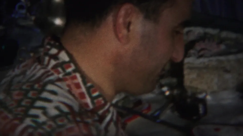 The home-movie frame shows a man leaning toward a table with dishes and glassware during a Westville, New Jersey gathering.