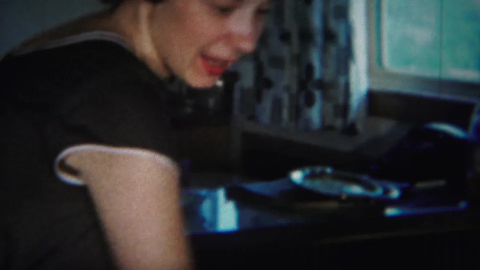A woman in a dark dress with white trim leans over a table near curtains and a window in the Westville home interior.