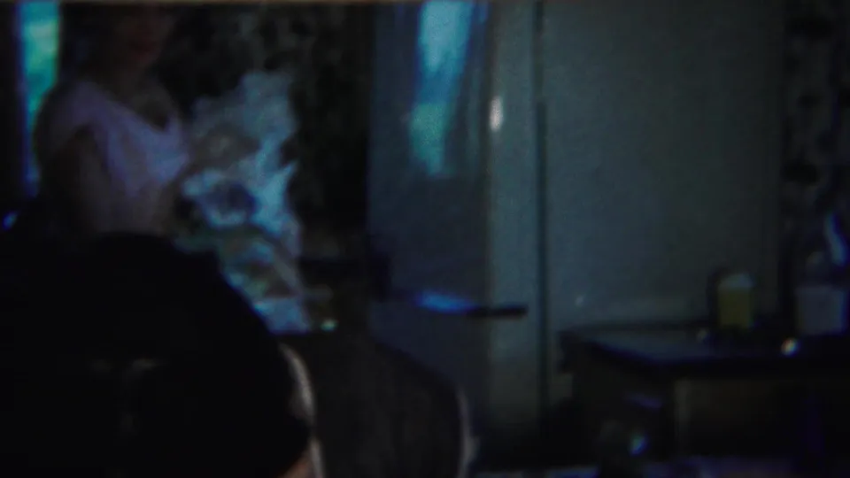 Inside the Westville home, a blurred man appears in the foreground as a woman is seen deeper in the kitchen area near a doorway or refrigerator.
