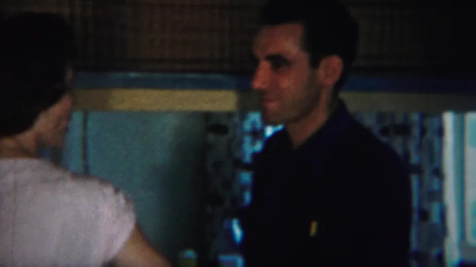 The man turns in profile toward the woman in a light dress, continuing a close conversation inside the Westville home.