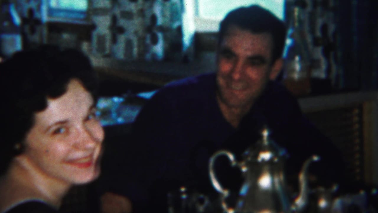 Woman smiling beside a man at a dining table with a silver teapot in front.