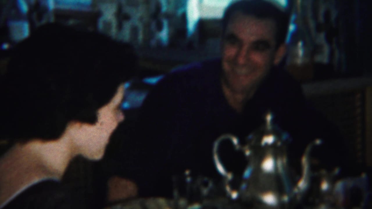 Woman turned toward a man across a table with a silver teapot and glassware.