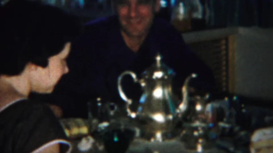 1951 Westville home-movie frame showing adults at an indoor dining table with cake, cups, and a silver-toned teapot.