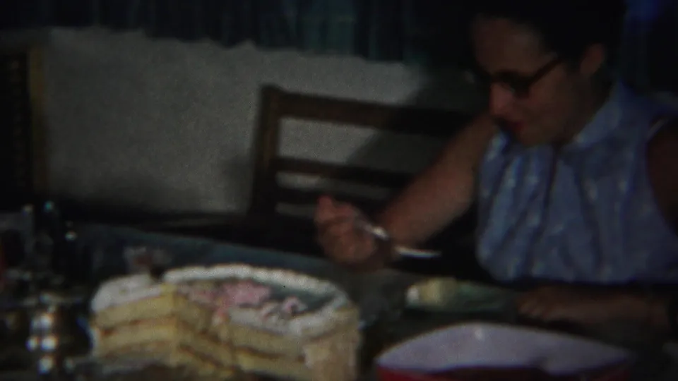 The woman looks down toward her fork and plate while eating cake at a dim Westville home table in 1951.